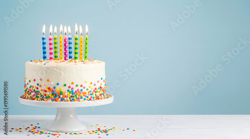 Colorful birthday cake with lit candles and sprinkles on blue background