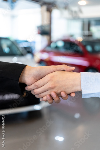 Close-up of a professional handshake in a car dealership. Successful vehicle purchase deal between dealer and client. Automotive sales and service concept. Vertical Shot