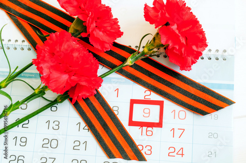 9 May background, red carnations and St George ribbon lying on the calendar with framed 9 May date, festive Victory day 9 May card