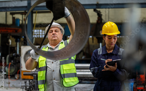 The supervisor inspects metal rings, the technician records the findings on a writing board in the industrial plant, quality control, and documentation.