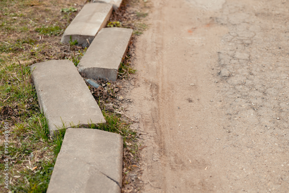 Obraz premium Concrete blocks line the edge of a dirt path while grass grows alongside. The scene depicts a simple outdoor setting that shows an interaction between natural and man-made elements