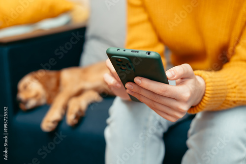 Fotografie A person sits on a couch and looks at their smartphone while a dog lies asleep beside them