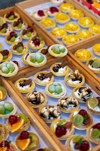 Assorted dessert cups with fruit and chocolate displayed in market stall, colorful sweet selection with orange kiwi grapes and mango, ready for sale in street food setting