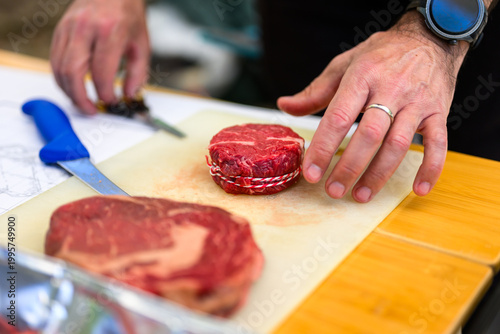 Close-up of a chef in black nitrile gloves precisely trimming a thick-cut ribeye steak with a sharp knife on a cutting board during a professional Steak Cookoff Association (SCA) BBQ competition.