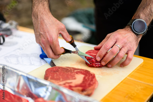 Close-up of a chef in black nitrile gloves precisely trimming a thick-cut ribeye steak with a sharp knife on a cutting board during a professional Steak Cookoff Association (SCA) BBQ competition.