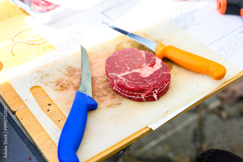 A perfectly trimmed and trussed raw ribeye steak sits on a wooden cutting board with a metal skewer, prepared for high-stakes professional grilling at a Steak Cookoff Association (SCA) BBQ competition