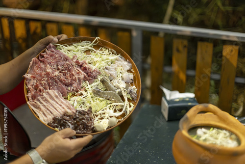 Konstfotografi Hand holding round tray of raw sliced pork and fresh cabbage for traditional hot