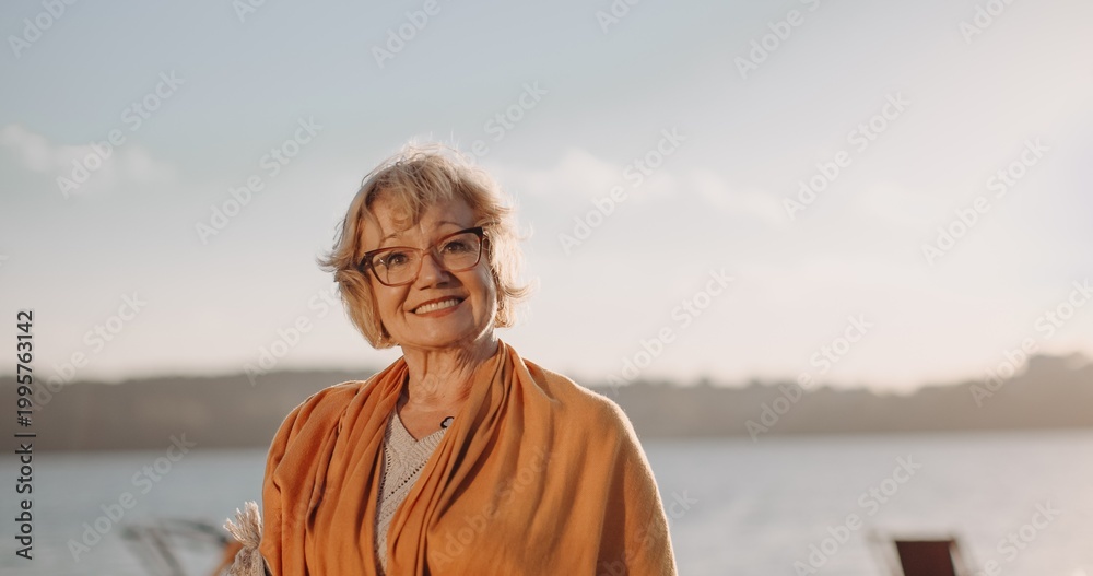 Fototapeta premium Senior woman smiling enjoying sunset by water