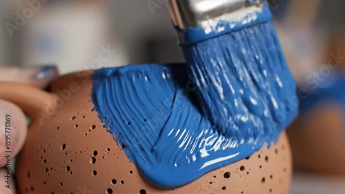 Close-up of a paintbrush applying vibrant blue paint to a terracotta pot