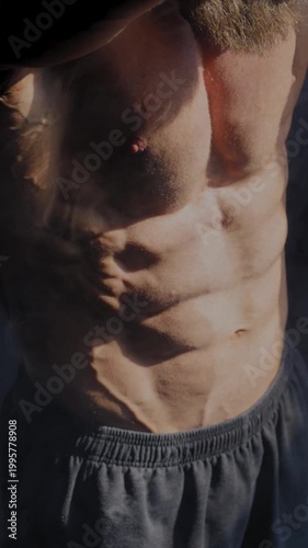 A male bodybuilder poses in shorts, showing off his muscles. Close-up of his chest and abs.