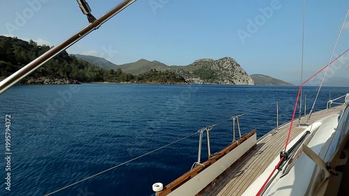 View from the wooden deck of a yacht with metal handrails onto the mountainous sea coast on a sunny day
