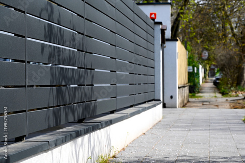 gray aluminum fence and gate. horizontal panels. narrow gaps.  powder coated finish. diminishing perspective view. modern fence design concept. concrete sidewalk. white stucco base and fence piers