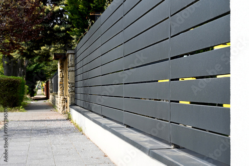 gray aluminum fence and gate. horizontal panels. narrow gaps.  powder coated finish. diminishing perspective view. modern fence design concept. concrete sidewalk. white stucco base and fence piers
