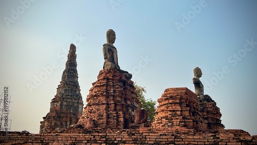 Ancient Buddha statues sitting on ruined brick pedestals with historic pagoda at Wat Chaiwatthanaram, the Unesco World Heritage site of Ayutthaya Historical park, Thailand.