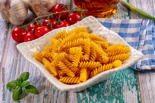 Tableau sur toile Dry fusilli pasta in white bowl, fresh cherry tomatoes, garlic, basil, rustic wo