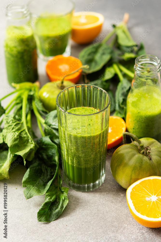 Fototapeta premium Fresh juice is made using spinach, chard, and broccoli along with oranges and tangerines. A glass of green juice sits by fresh ingredients on a clean kitchen counter