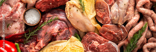 Various cuts of meat are arranged on a dark surface. Beef steaks, quail, pork sausages, turkey, chicken, and pork are present along with herbs and spices, banner