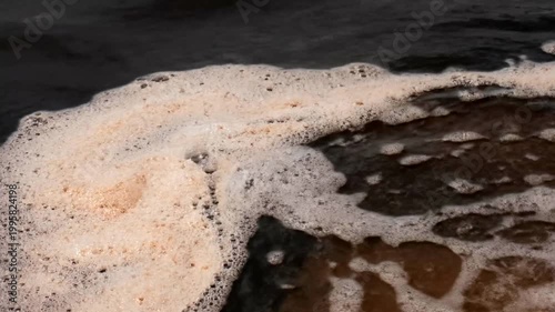 Natural foam floating on dark polluted river water surface.