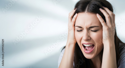 Young woman screaming with eyes closed and hands on head, expressing extreme stress concept, emotional pain, and mental health crisis.