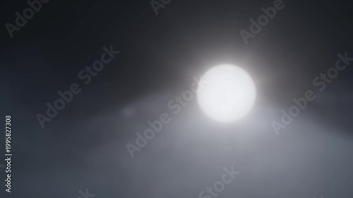 Bright full moon shining through thick dark moving clouds in night sky at midnight.