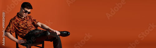 Cuadro en lienzo Handsome young man poses stylishly while sitting on a chair against a vibrant or