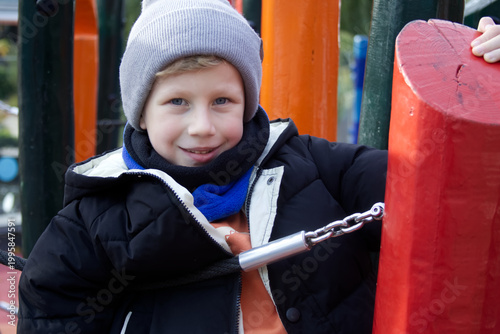 Smiling Boy in Beanie and Winter Jacket on Colorful Playground