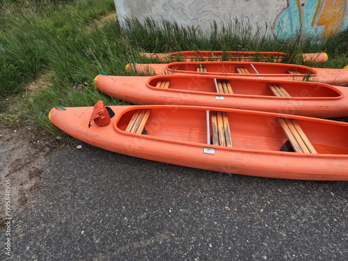 Group of orange plastic recreational canoes resting on a grassy riverbank, outdoor water sports and summer camp equipment.