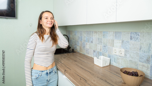 Happy young woman talking on smart phone in kitchen at home