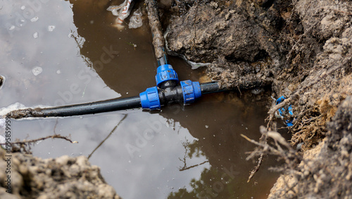 Underground water pipe with blue plastic compression fittings submerged in muddy flooded excavation pit, water leak repair, plumbing emergency, or utility infrastructure maintenance