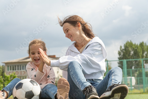 Woman sitting on grass with her daughter at sport field