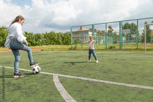 Woman playing soccer ball with her daughter at sport field
