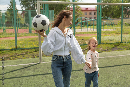 Woman playing soccer ball with her daughter at sport field