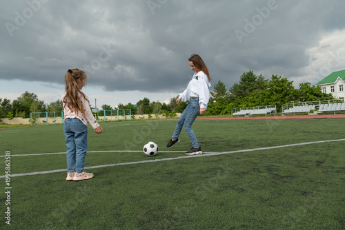 Woman teaching her daughter soccer ball at sport field