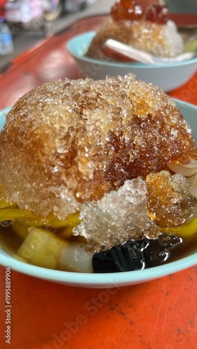 Thai - Chinese shaved ice dessert called Bok Kia, topped with longan syrup red daed, and chewy rice noodles in bowl.