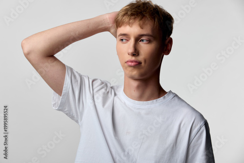 Fotografie Thinking man in a casual white tee scratching his head, conveying curiosity, dou