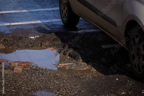 Urban scene with car passing by a big pothole in the asphalt
