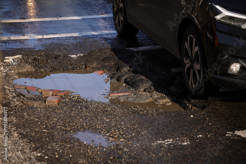 Urban scene with car passing by a big pothole in the asphalt