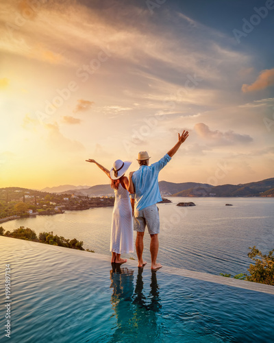 Canvas Print A happy couple on summer vacation standing by the swimming pool enjoys a beautif