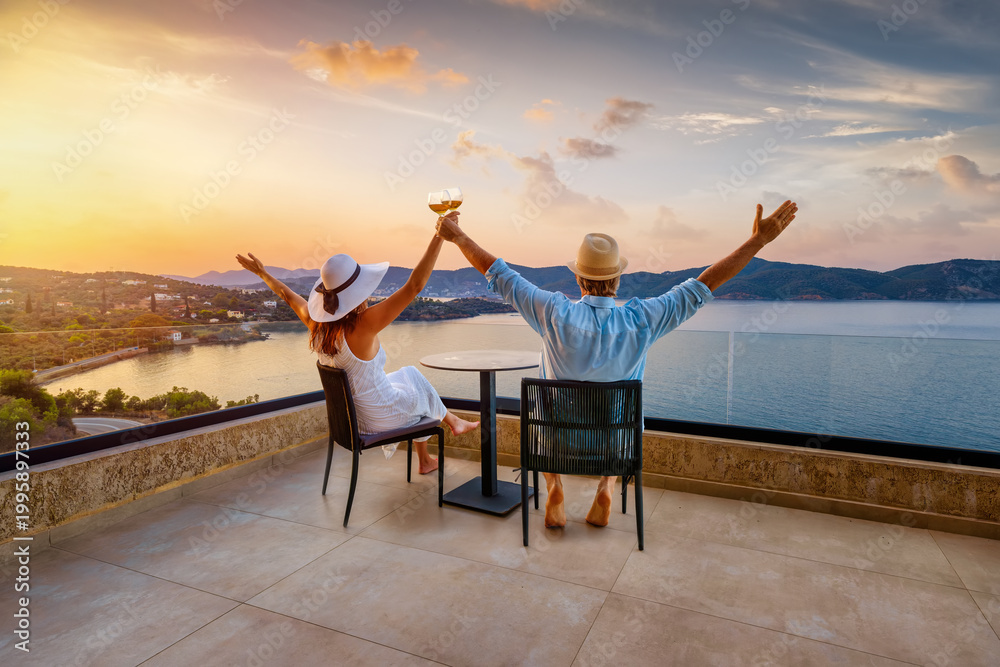 Fototapeta premium A happy holiday couple enjoys the beautiful summer sunset in the mediterranean sea with a glass of wine as a concept for romantic travel
