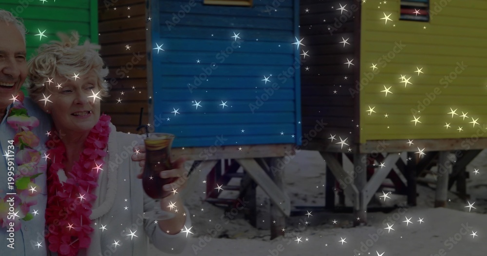 Fototapeta premium Standing couple wearing pink, rainbow leis holding tiki glass by colorful huts on sand, copy space