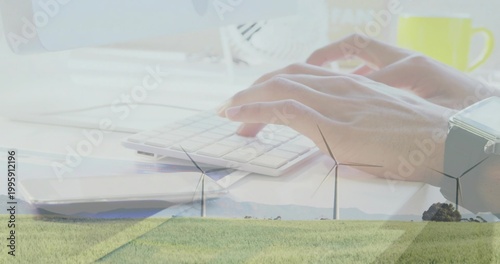 Typing adult hands resting on small keyboard at pale desk, merging with wind turbines, mug, watch