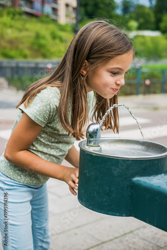 фотографія Thirsty child leaning over a metal water fountain to drink on a hot summer day,