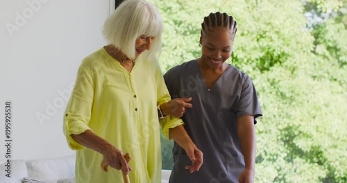 Senior with African American nurse guiding senior using cane near window to assist walking