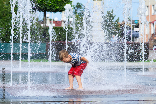 Photography Child playing with water fountain in city square on summer day