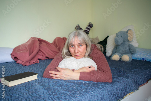 Senior woman lying on bed looking directly at camera with serious expression