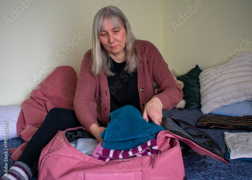 Senior woman placing folded clothes into suitcase preparing for travel