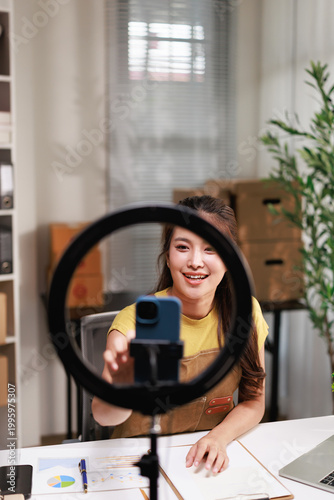 Obraz na płótnie Asian female entrepreneur streaming live video with smartphone and ring light, c