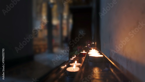 Foto Row of lit candles along church wall with blurred figures in background, creatin
