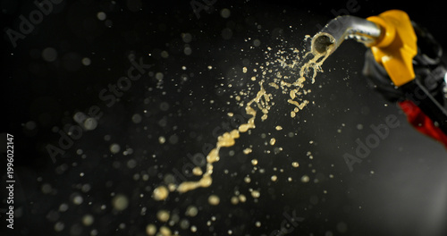 Fotografie Gasoline jet spraying from fuel nozzle held by hand on dark background