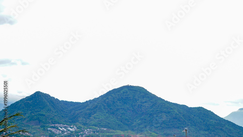 A serene rural landscape featuring a lush green mountain under a bright sky, with farmland in the foreground and scattered trees across the countryside.